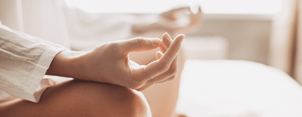 Close up shot of a person's hands resting on their knees, palms upward in a meditative pose