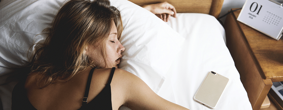 A woman lying on her stomach in bed with her phone next to her, and a bedside calendar reading January 1