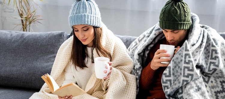 People wrapped in blankets holding hot drinks to stay warm in the winter