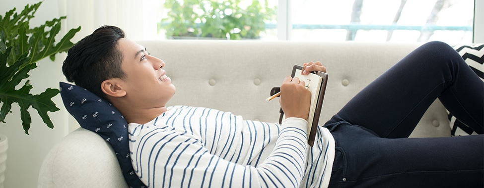 Man lying on his back with a journal in his lap and pencil in hand, smiling