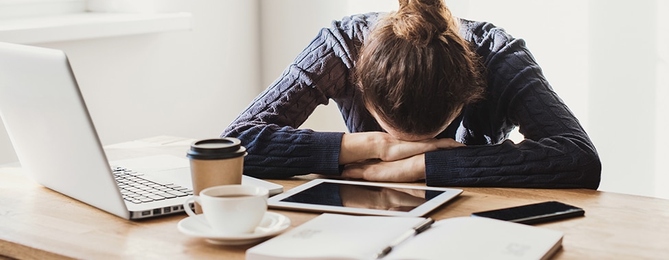 Woman feeling burnout at her desk, resting her head on her hands