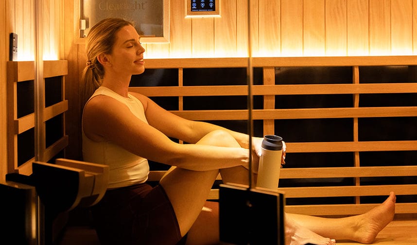 Woman sitting in a sauna while stretching holding a waterbottle.